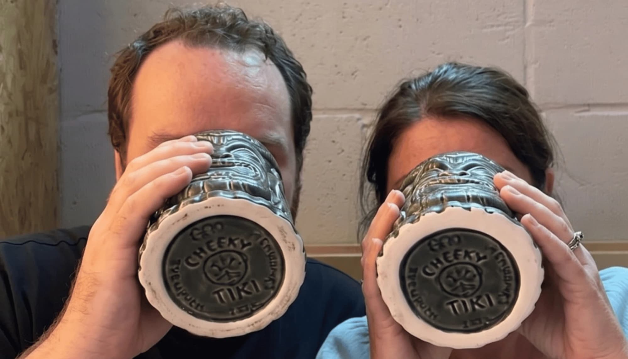 Jason and Angela drinking from Cheeky Tiki mugs, faces hidden behind them